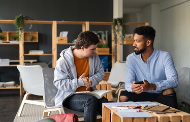 Young happy man with Down syndrome and his tutor studying indoors at school.