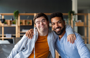 Young man with Down syndrome and his tutor with arms around looking at camera indoors at school - obrazy, fototapety, plakaty