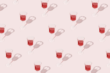 Minimal pattern made of wine glasses with red wine isolated on pastel pink background. Drink for party, wine shop or wine tasting concept. Sun, shadows and reflections. Summer Mediterranean texture. 