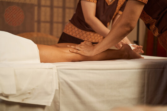 Experienced masseuses performing four-hand leg massage on customer