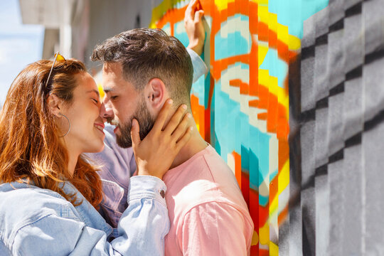 Couple kissing by grafitti wall during sunny day
