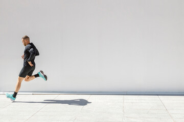 Young male athlete running by white wall