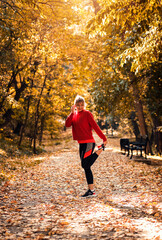 Fototapeta premium Young woman warming up and stretching before running in park.