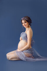 beautiful glamorous caucasian pregnant girl in fabric on a blue background. Isolate