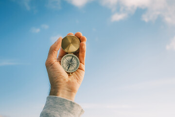 Travel concept. Vintage compass in male hands against the blue sky.