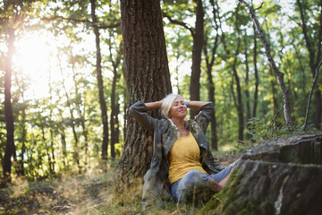 Portrait of senior woman relaxing and sitting with eyes closed outdoors in forest.