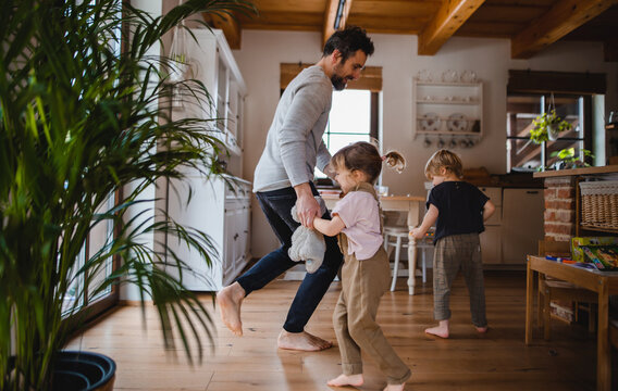 Mature father with two small children dancing indoors at home.