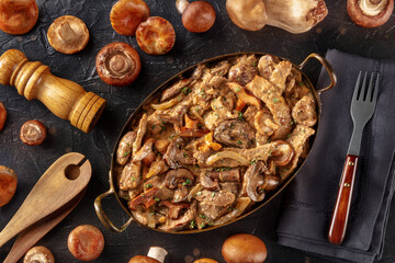 Beef stroganoff, mushroom and meat ragout with cream sauce, in a cooking pan with ingredients, overhead flat lay shot on a black slate background