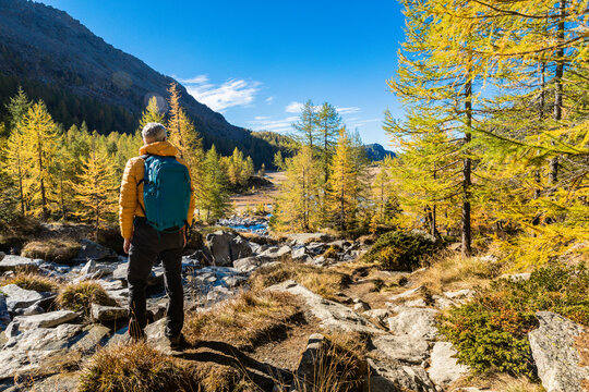 Mature male hiker with backpack looking at mountains during autumn in Val Masino, Sondrio, Italy
