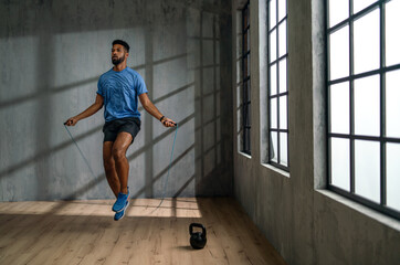 Young African American sportsman using jumping rope indoors, workout training concept.