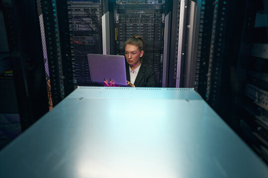 Woman network engineer using laptop while working in server room
