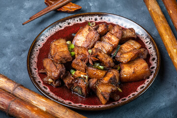 Braised pork belly according to the traditional recipe of local Chinese cuisine, close-up. Dark background, Chinese food.