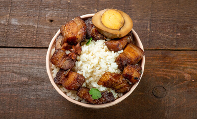 Bowl with rice and braised pork belly in Chinese style on a wooden background, top view. Free space.