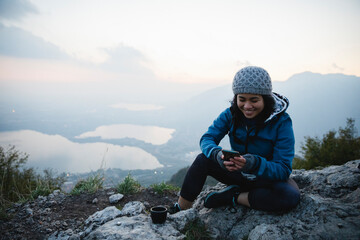 Happy young woman text messaging through smart phone on mountain