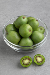 Glass bowl with fresh whole and halved kiwi berries close up  