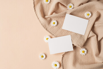 Blank paper sheet card with mockup copy space, chamomile flower buds and muslin cloth on neutral beige background. Minimal aesthetic business brand template. Flat lay, top view