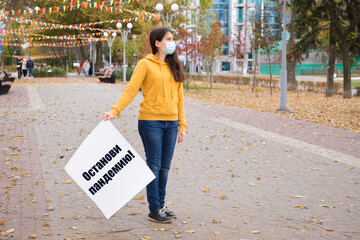 Masked woman holding a poster with text on Russian, translated from Russian Stop the pandemic