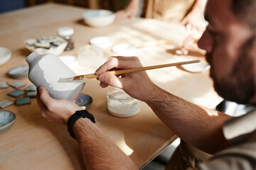 Close up of bearded male artist decorating ceramics in pottery workshop, copy space