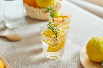 Fototapeta premium Citrus and rosemary fresh lemonade in glass on a white table at home, summer drink, detox healthy water.