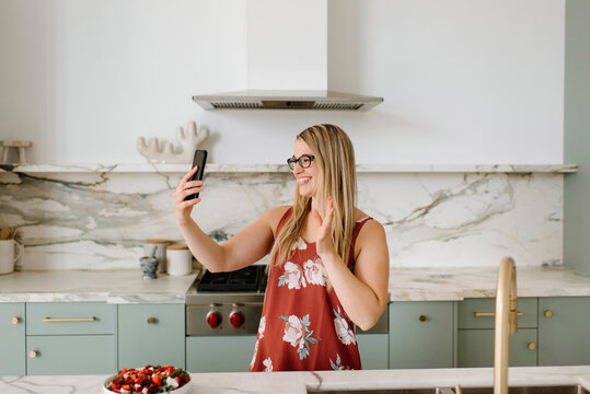 Female nutrient expert waving hand during video call through smart phone in kitchen