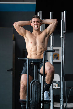Tired male athlete with hands behind head sitting on cross trainer in gym