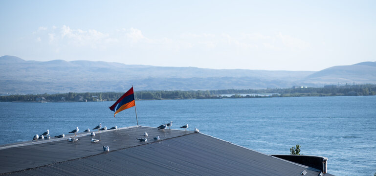 Panoramic shot of birds perched on a roof with Armenian flag on the bay of Lake Sevan in Armenia