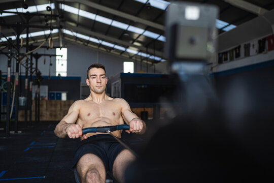 Shirtless sportsman exercising on rowing machine in gym
