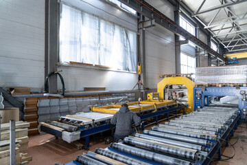 Warehousing of finished products. Conveyor belt or line with packaged metal roof tiles inside workshop using crane. Industrial production of roofing on automated equipment.