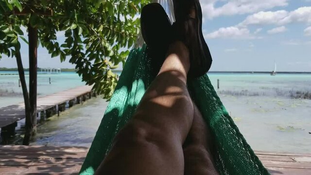 A video from low angle shot of a male relaxing in a hammock at Bacalar Lagoon, Mexico