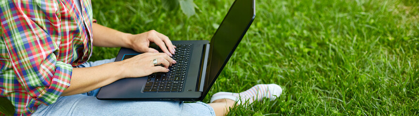 Banner Woman freelancer in casual clothes with her computer laptop sitting on the grass at the park