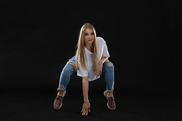 Young dancer on bent legs, propping herself up with one hand and looking at the camera. Long blonde hair.