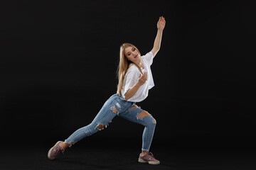A young dancer is performing a pose from a dance routine while standing wide apart, facing the camera. Long blonde hair.