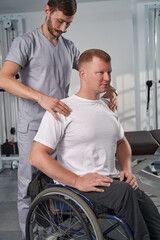 Caucasian doctor checks shoulders of patient with spinal cord injury - obrazy, fototapety, plakaty