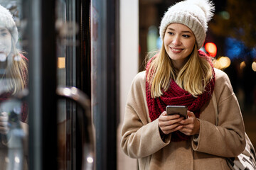 Portrait of beautiful happy young woman calling on smartphone over christmas light in winter evening