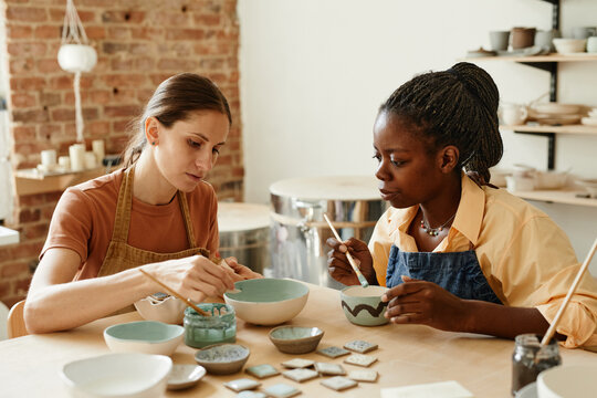Warm toned portrait of two young women enjoying pottery workshop in cozy studio, copy space