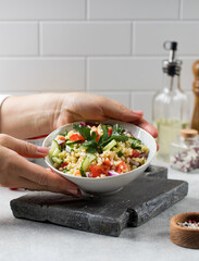 A hand squeezes the juice from a lemon into a vegetarian salad of bulgur and vegetables. Oriental cuisine