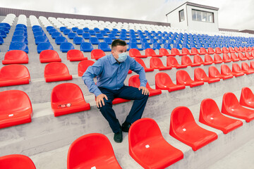 lonely man with a protective mask on his face is sitting and watching a sports competition alone on...