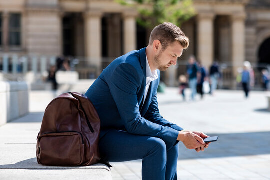 Male professional using mobile phone while sitting by backpack