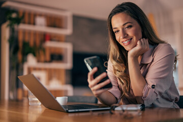 Smiling woman reading text message while working at home