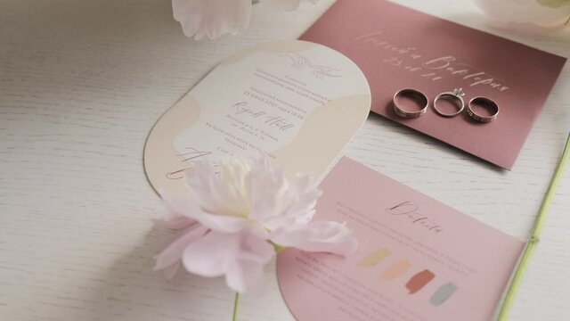 white pions bouquet and wedding rings lying on the invitation card