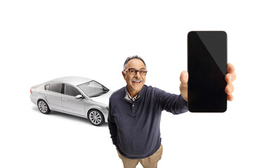 Cheerful mature man showing a smartphone and standing in front of a car