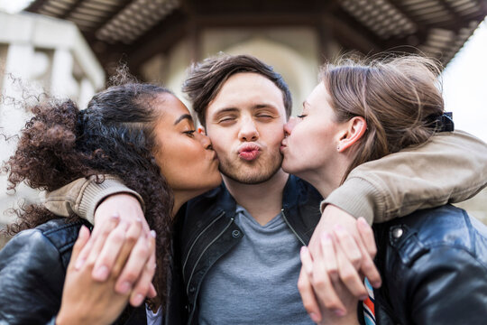 Young women kissing cheeks of man with puckered lips
