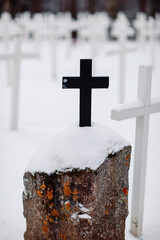 Old catholic cemetery with white wooden crosses in snow. Black cross among white crosses.