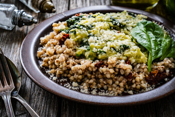 Boiled white buckwheat groats, sun dried tomatoes, parmesan and spinach served on wooden table

