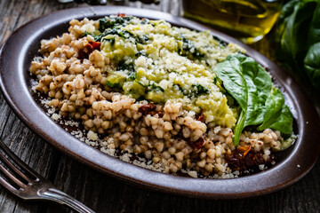Boiled white buckwheat groats, sun dried tomatoes, parmesan and spinach served on wooden table
