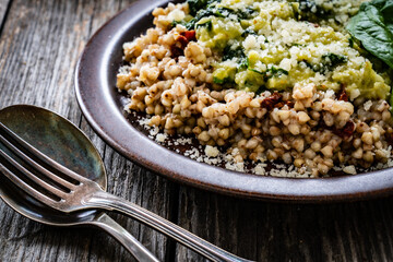 Boiled white buckwheat groats, sun dried tomatoes, parmesan and spinach served on wooden table

