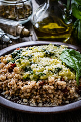 Boiled white buckwheat groats, sun dried tomatoes, parmesan and spinach served on wooden table
