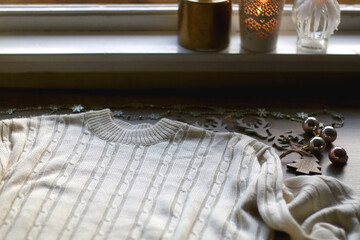 White cable knit sweater and various Christmas decorations on wooden background. Selective focus.