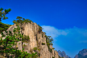 High granite mountains with green trees, blue sky and white clouds. Landscape of Mount Huangshan (Yellow Mountain). UNESCO World Heritage Site. Anhui Province, China.