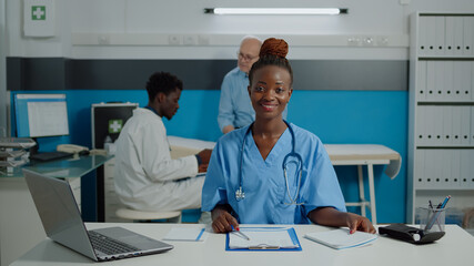 Obraz premium Close up of woman working as nurse sitting at desk and reading documents, files, papers of patient checkup. Person wearing uniform and stethoscope in healthcare cabinet at facility